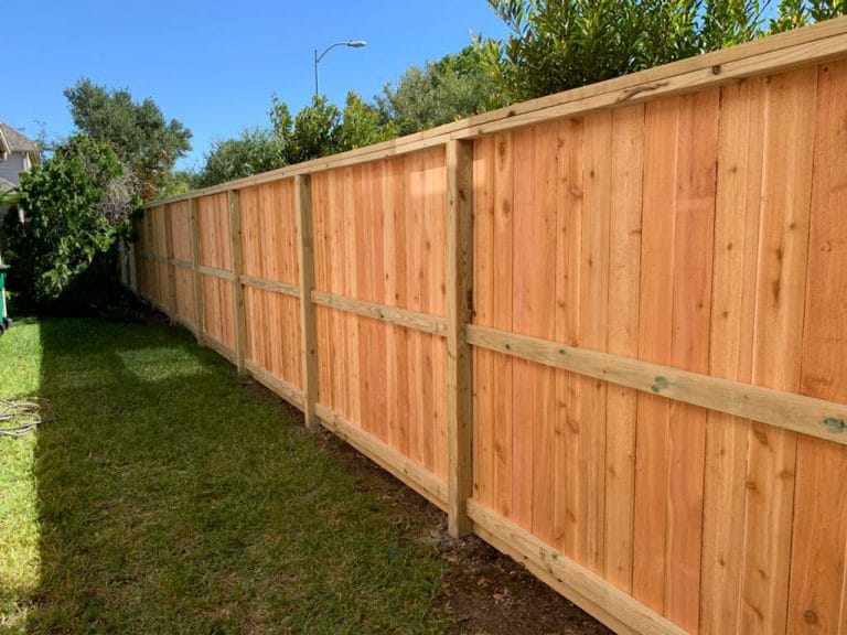 New wood privacy fence with its rails and posts facing a side yard