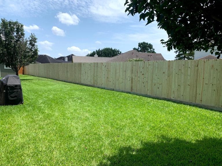 Long new wood privacy fence across the back of a grassy yard
