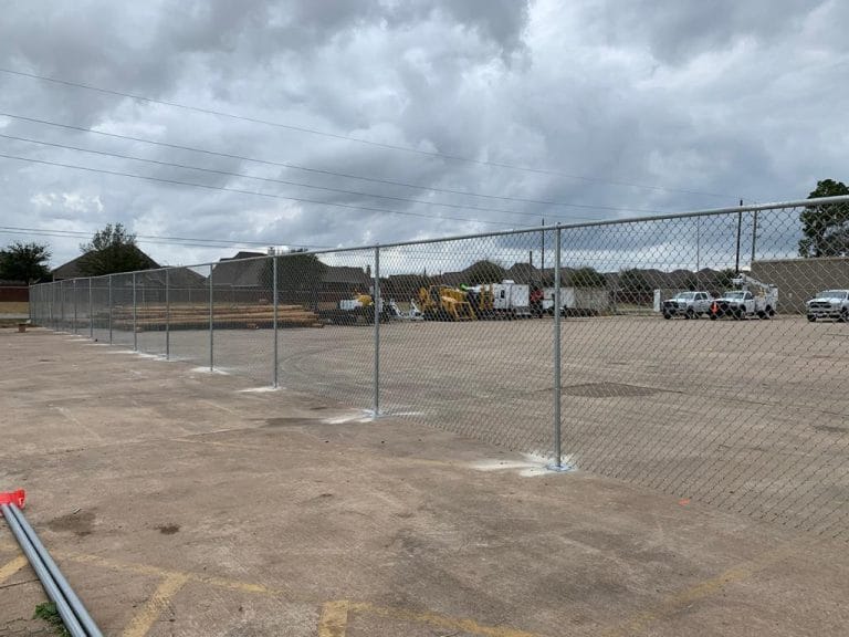 New galvanized chain link fence line with posts set across a large paved lot