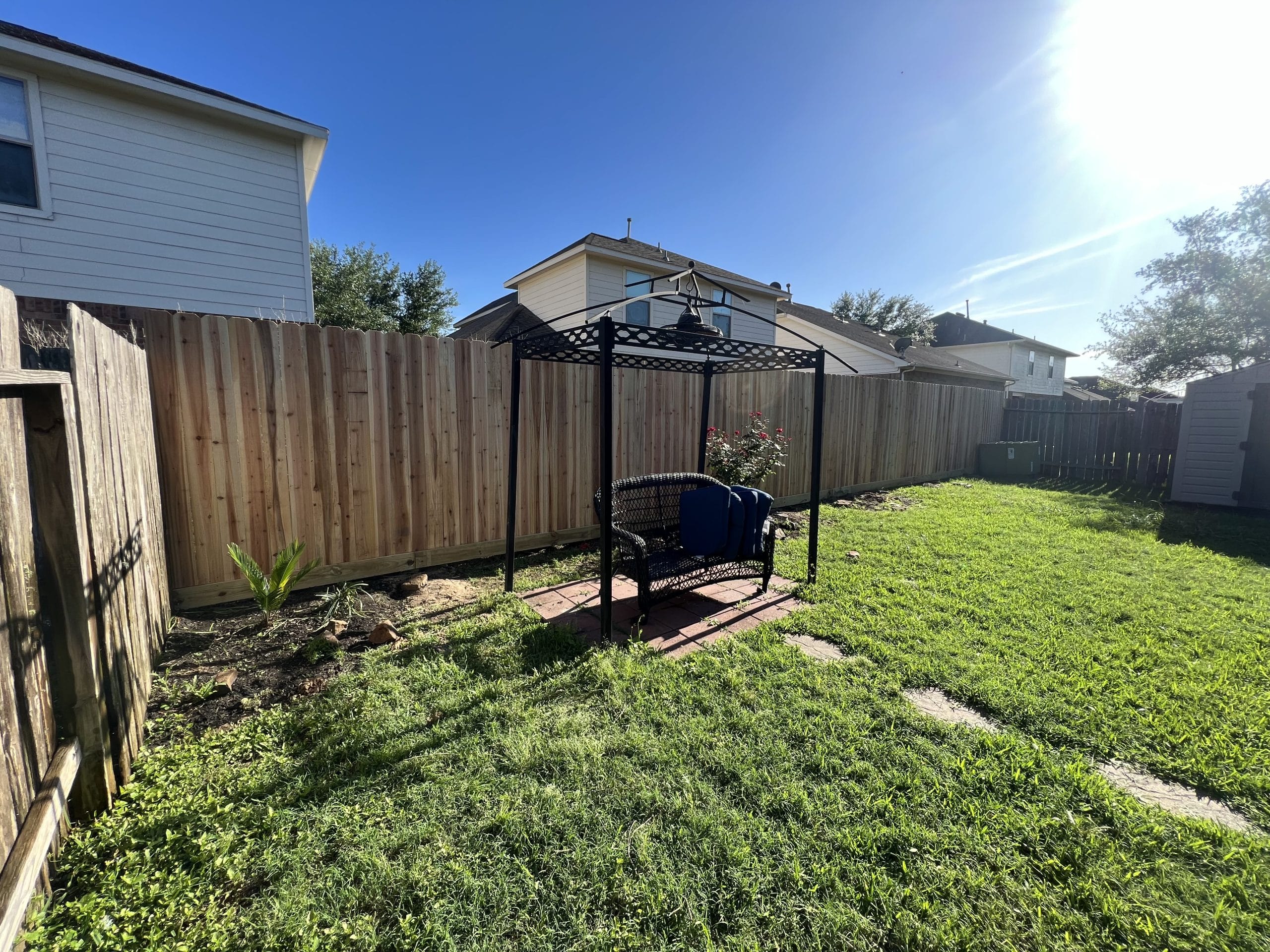 Wood privacy fence around a grassy Kemah backyard with a canopy swing on a brick pad