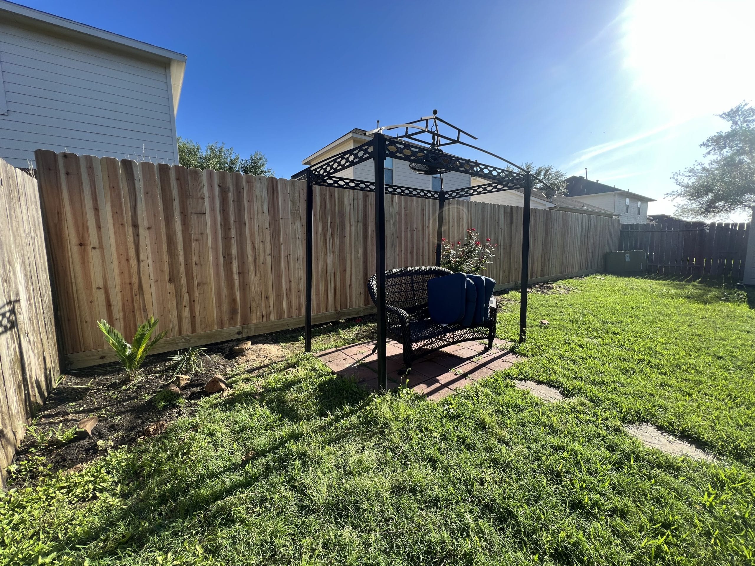 Backyard wood privacy fence line behind a canopy swing and garden bed in Kemah