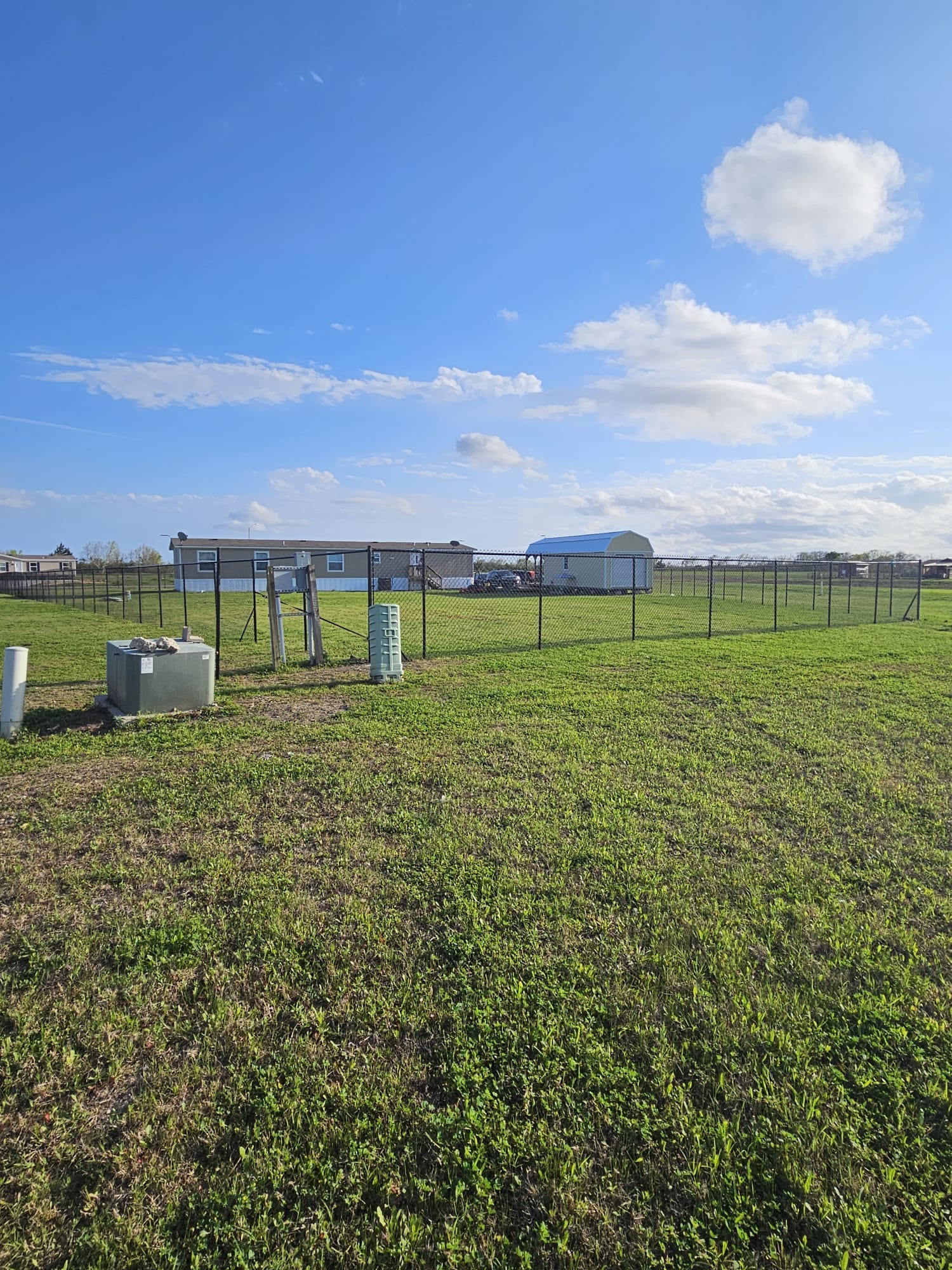 Chain link fence crossing a large open grass field beside an industrial building
