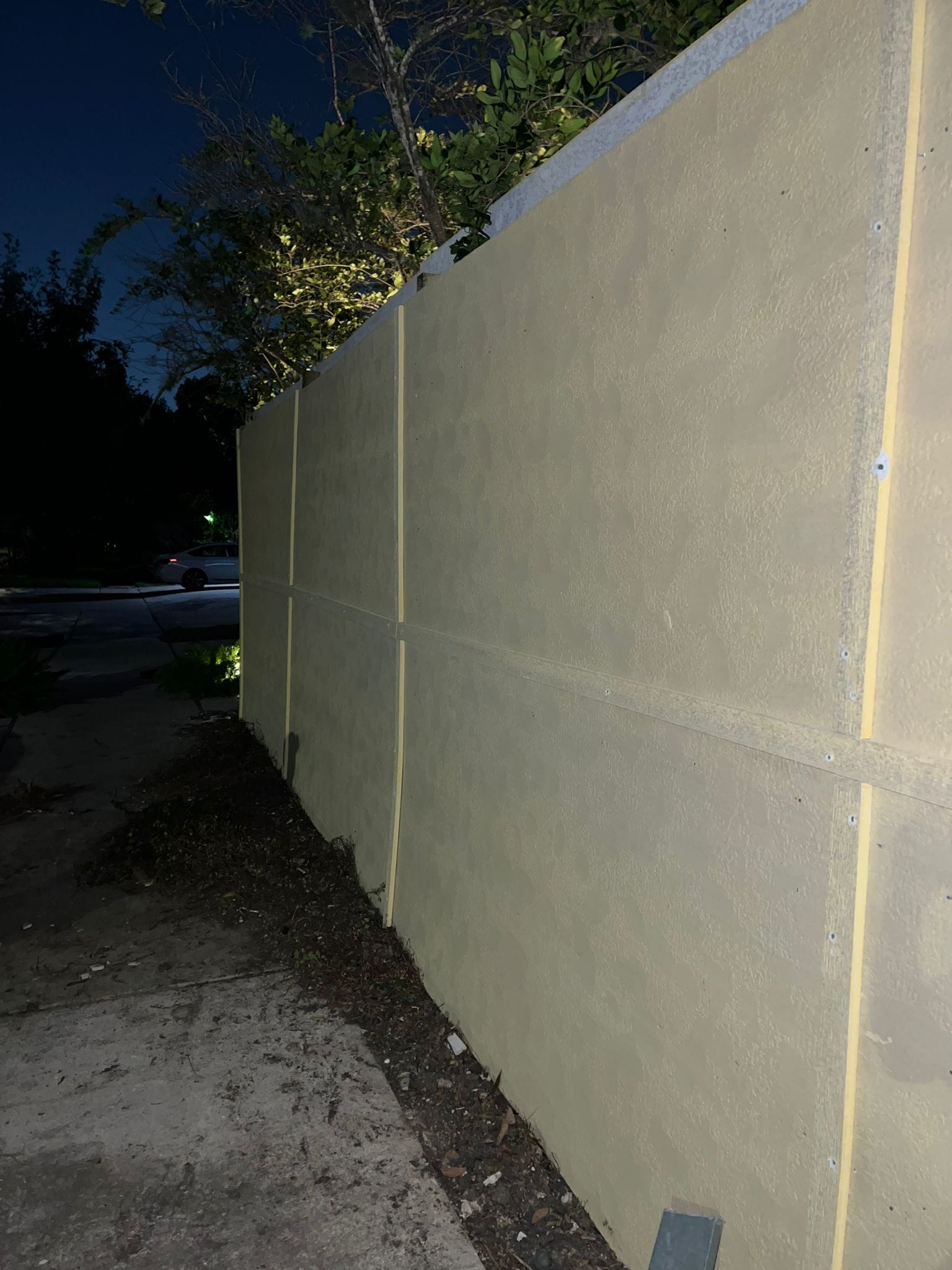 Tall smooth-faced solid fence photographed after dark in League City