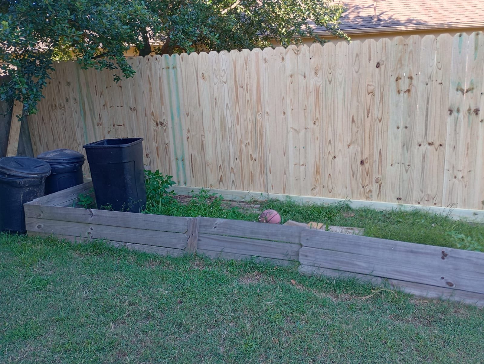 Wood privacy fence behind a raised timber planter and bins