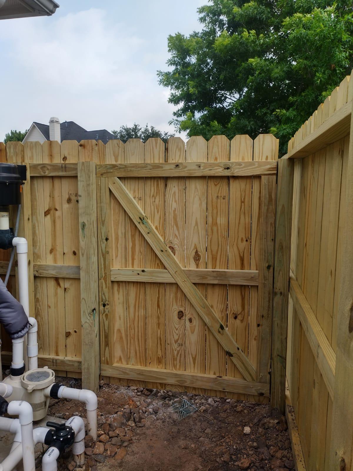 Braced pressure-treated pine walk gate closed in a privacy fence beside swimming pool pump and filter pipework