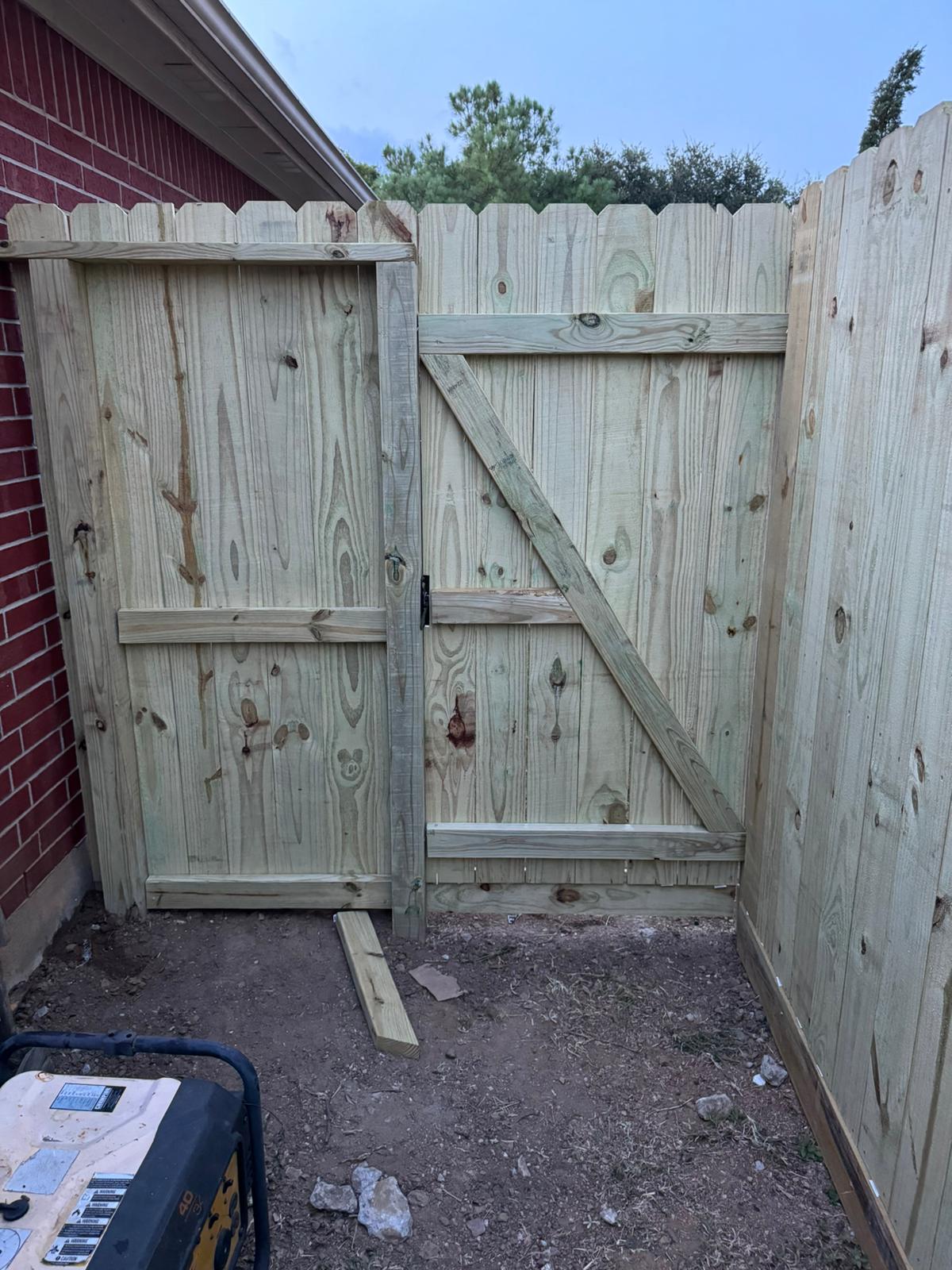 Wide new wood double gate with diagonal braces, set between a red brick house and a new pine privacy fence