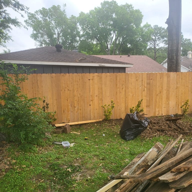 Newly built pine privacy fence across a backyard with the torn-out old fence lumber stacked in the foreground