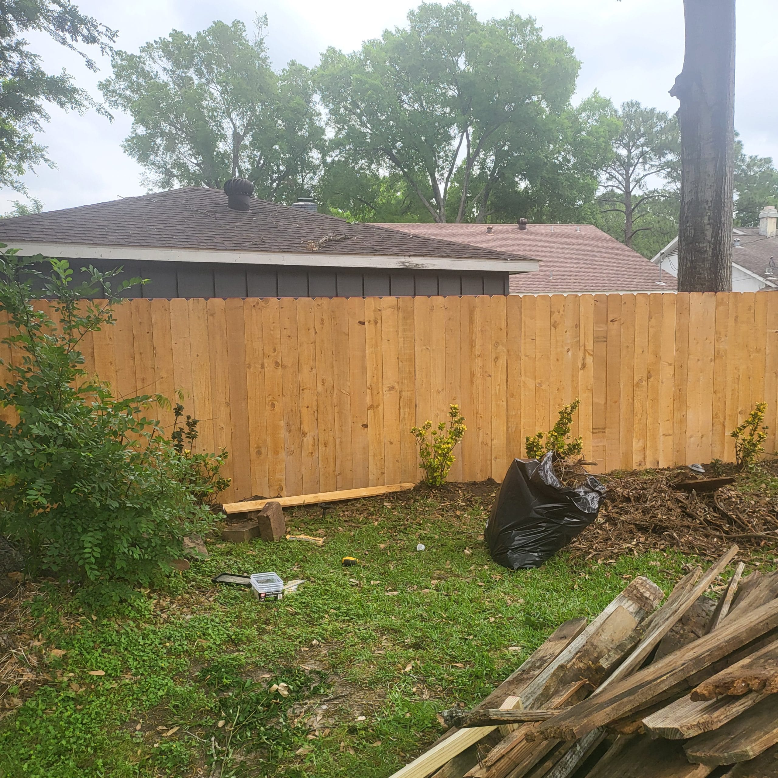 Completed pine privacy fence across a backyard, with torn-out lumber stacked nearby