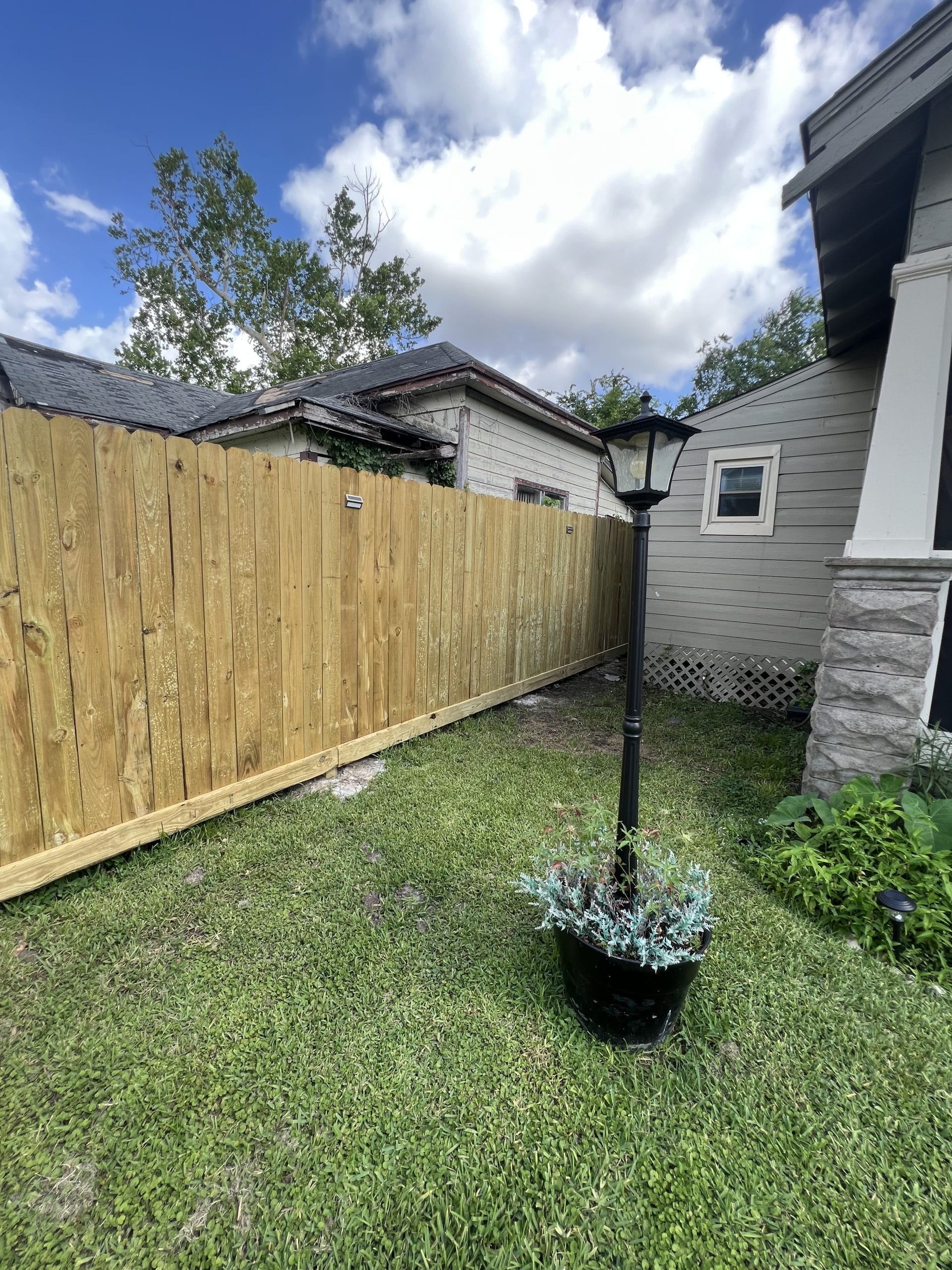 Pine privacy fence enclosing a backyard lawn beside a house with a lamp post