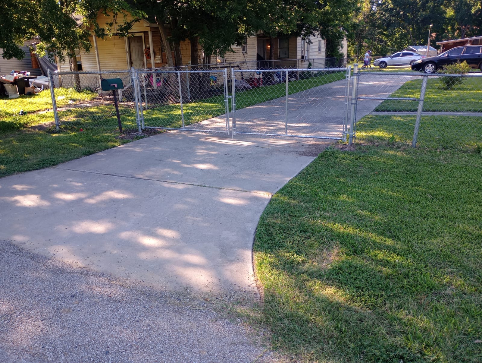 Galvanized chain link double swing gate closed across a concrete residential driveway, with chain link fence running to each side