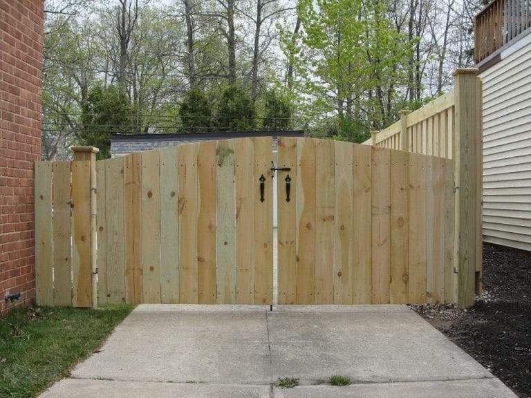 Arched double wood gate closing off a concrete driveway