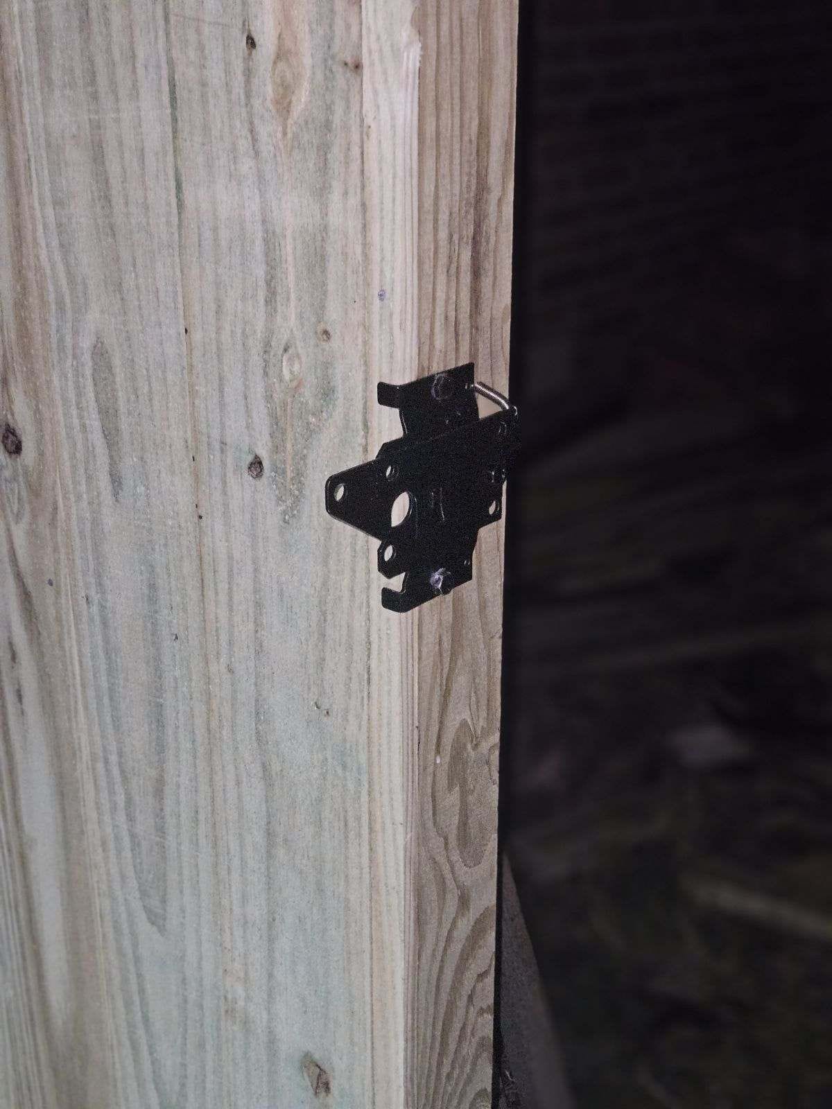 Close-up of a black gate hinge fixed to a wood post