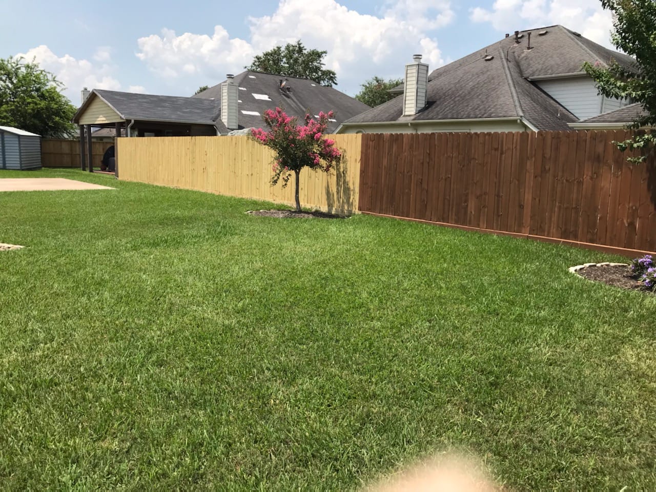 New pale pine privacy fence meeting an older stained wood fence at the corner of a large back lawn, with houses beyond