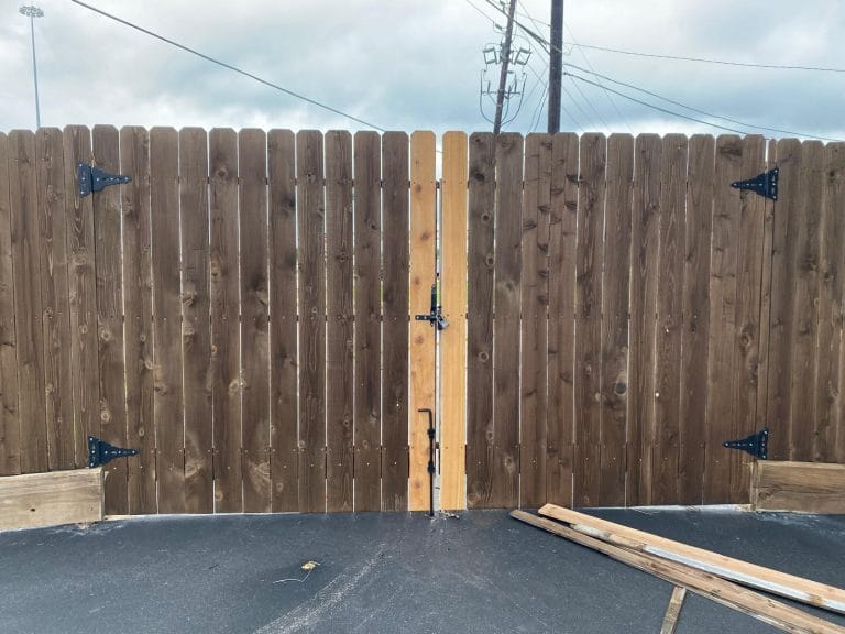 Stained wood double drive gate with black strap hinges and a cane bolt on a commercial lot