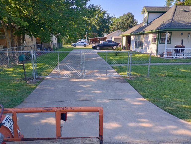 Galvanized chain link fence along a residential lawn with a gate across the concrete drive