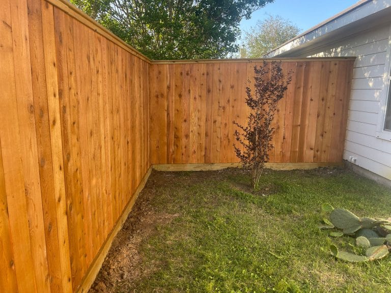 Wood privacy fence forming a corner around a lawn with a young tree