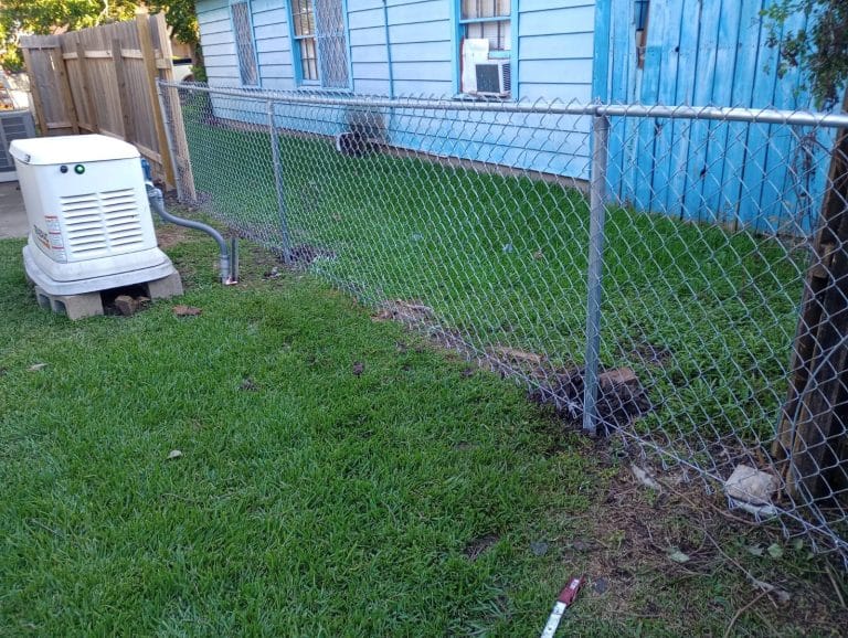 Galvanized chain link fence beside a standby generator and a blue house