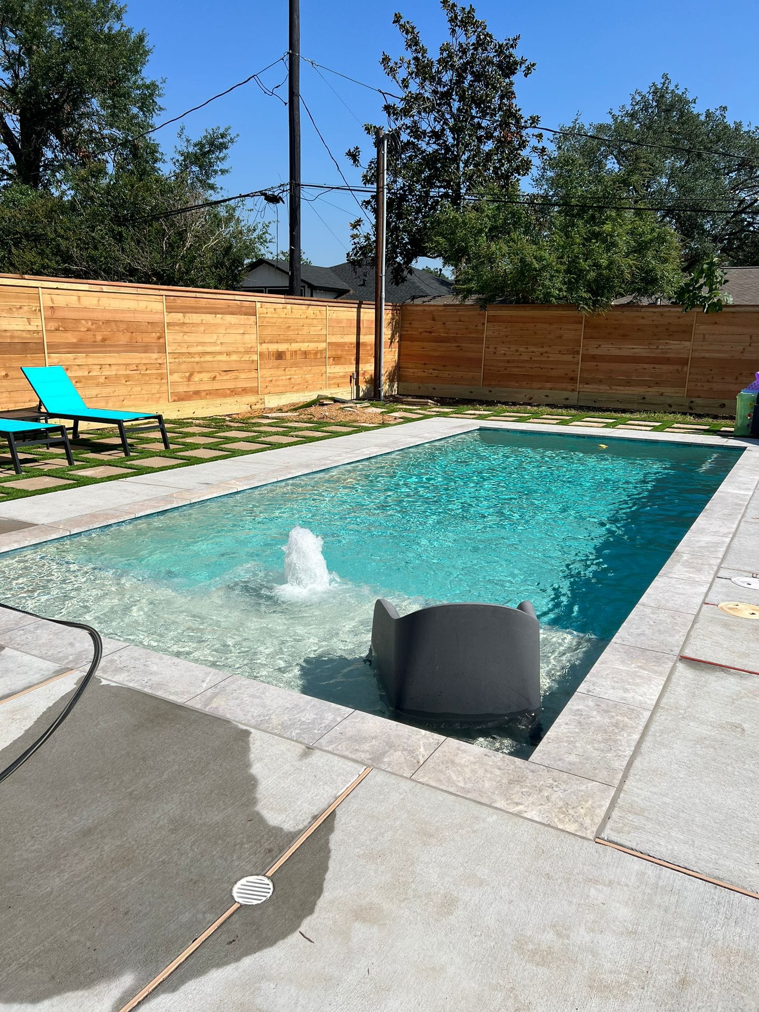 New rectangular swimming pool with a bubbler and pale coping, a turf-and-paver patio with turquoise loungers, and a tall horizontal cedar privacy fence along the back and side of the yard