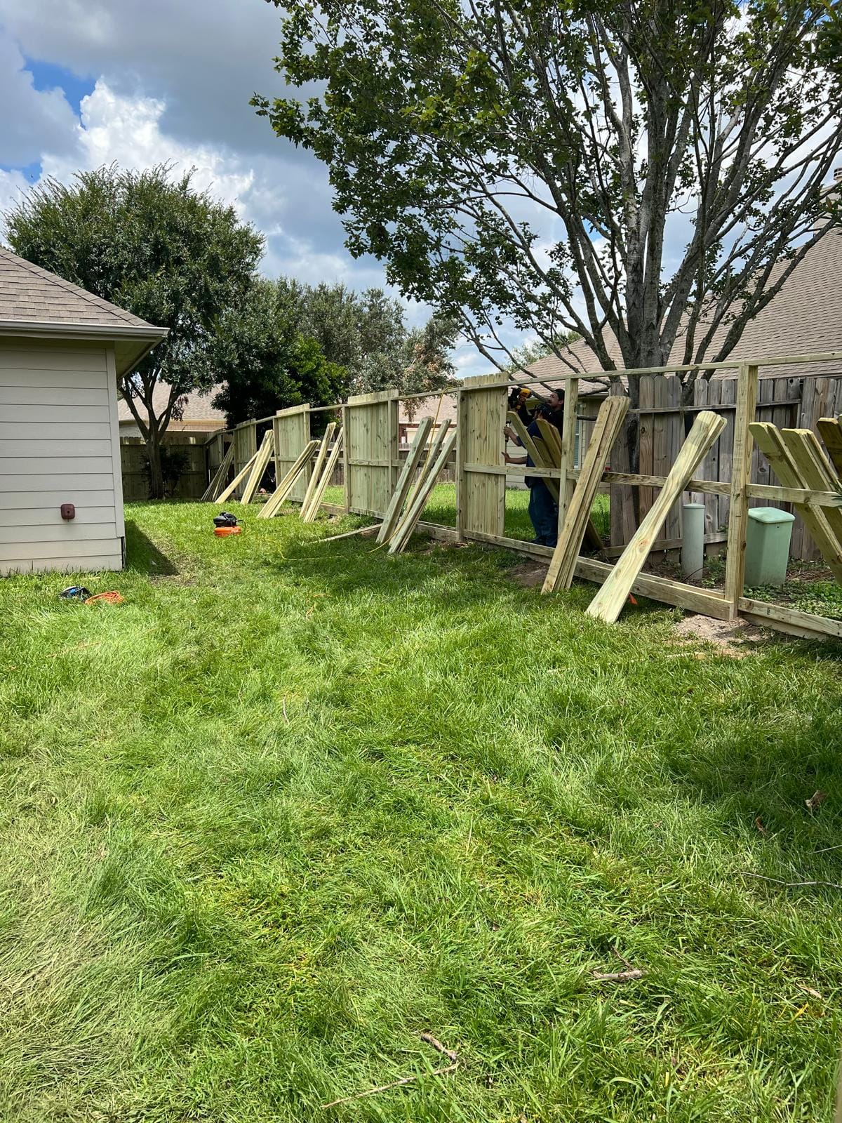 A new wood fence being framed between two back yards, with posts braced by diagonal boards and a house at the left