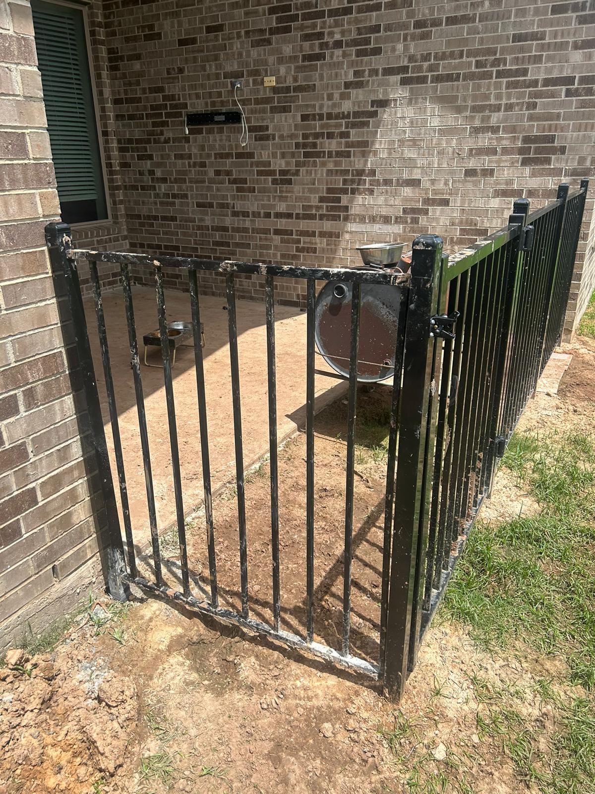 Black metal-framed double driveway gate with wood infill pickets and an arched top with finials, on a dirt drive