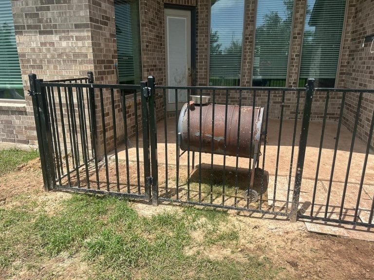 Black metal fence panels enclosing equipment beside a brick building
