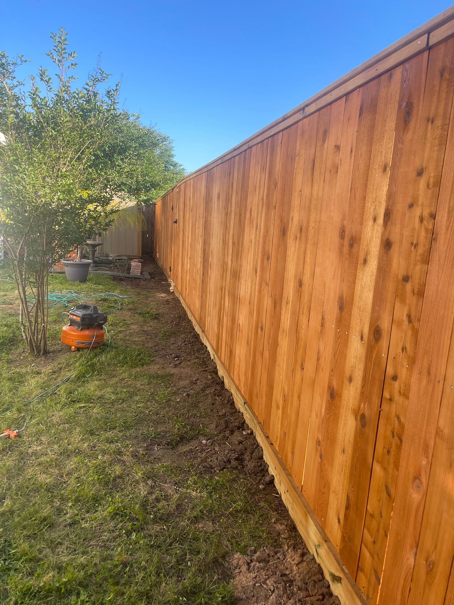 Red-stained cedar privacy fence running along a lawn