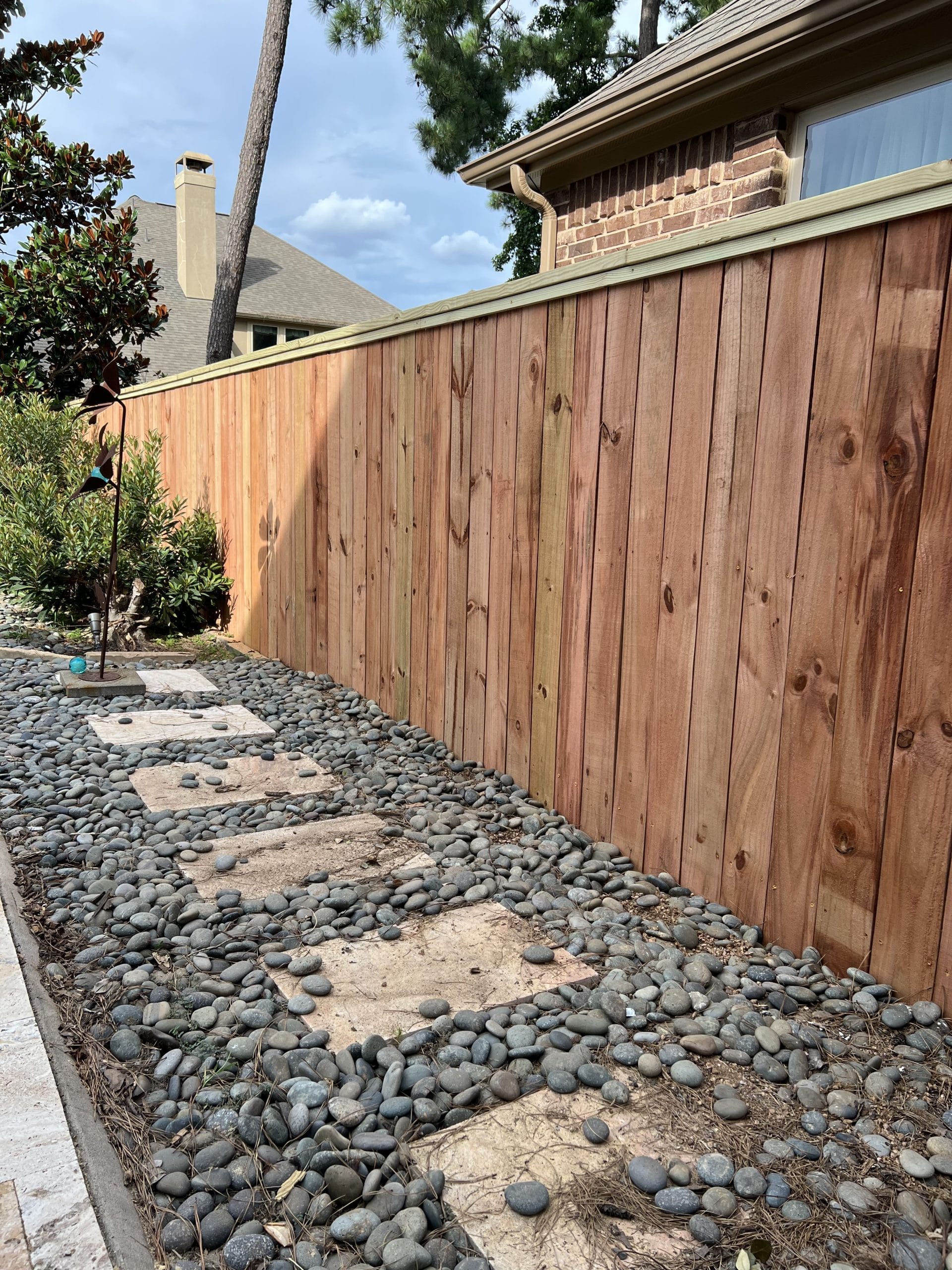 Stained wood privacy fence with a top cap beside a stepping-stone path, next to a pool patio
