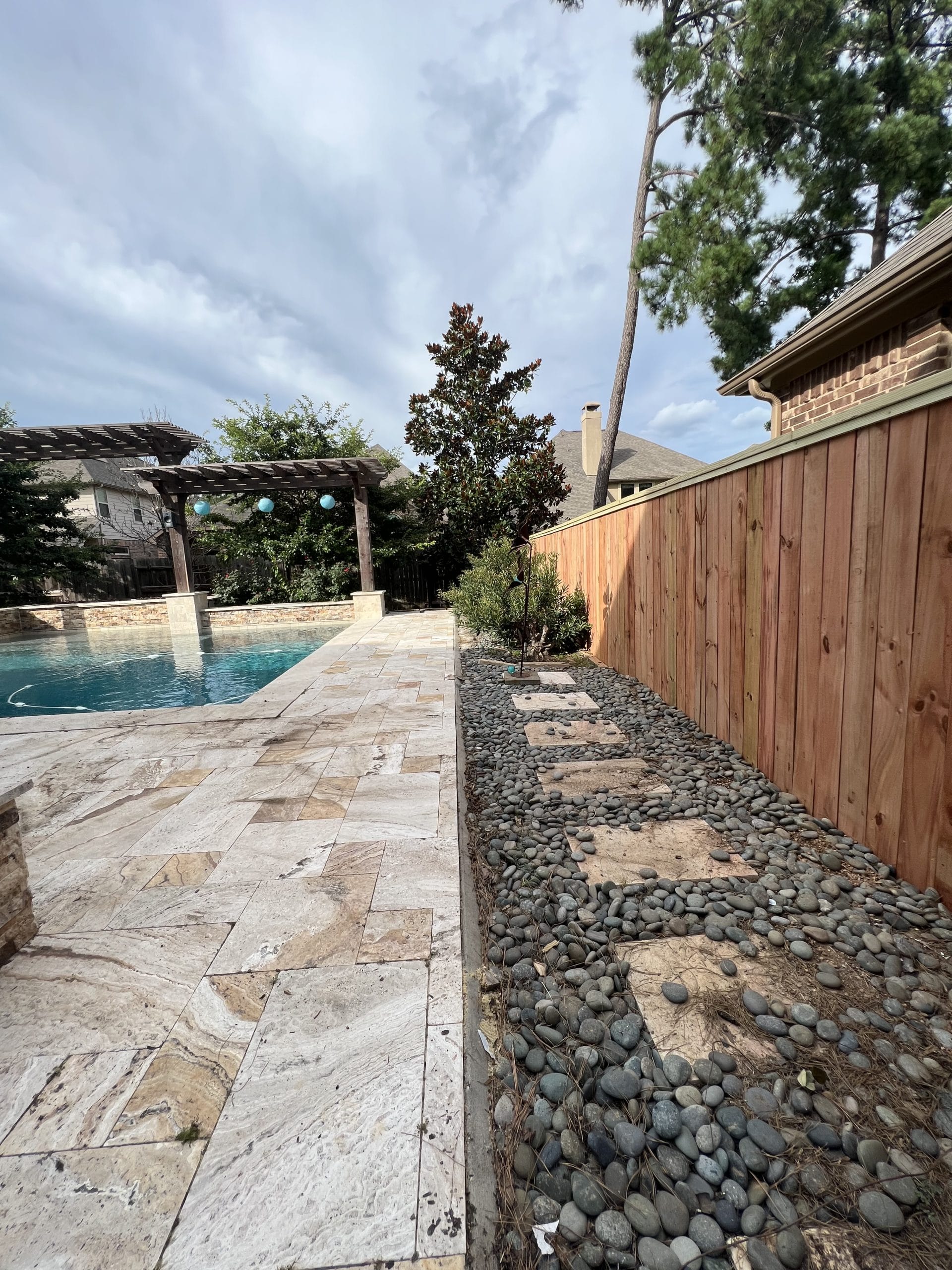 New cedar-toned wood privacy fence along a travertine pool patio, with a pergola and magnolia tree beyond