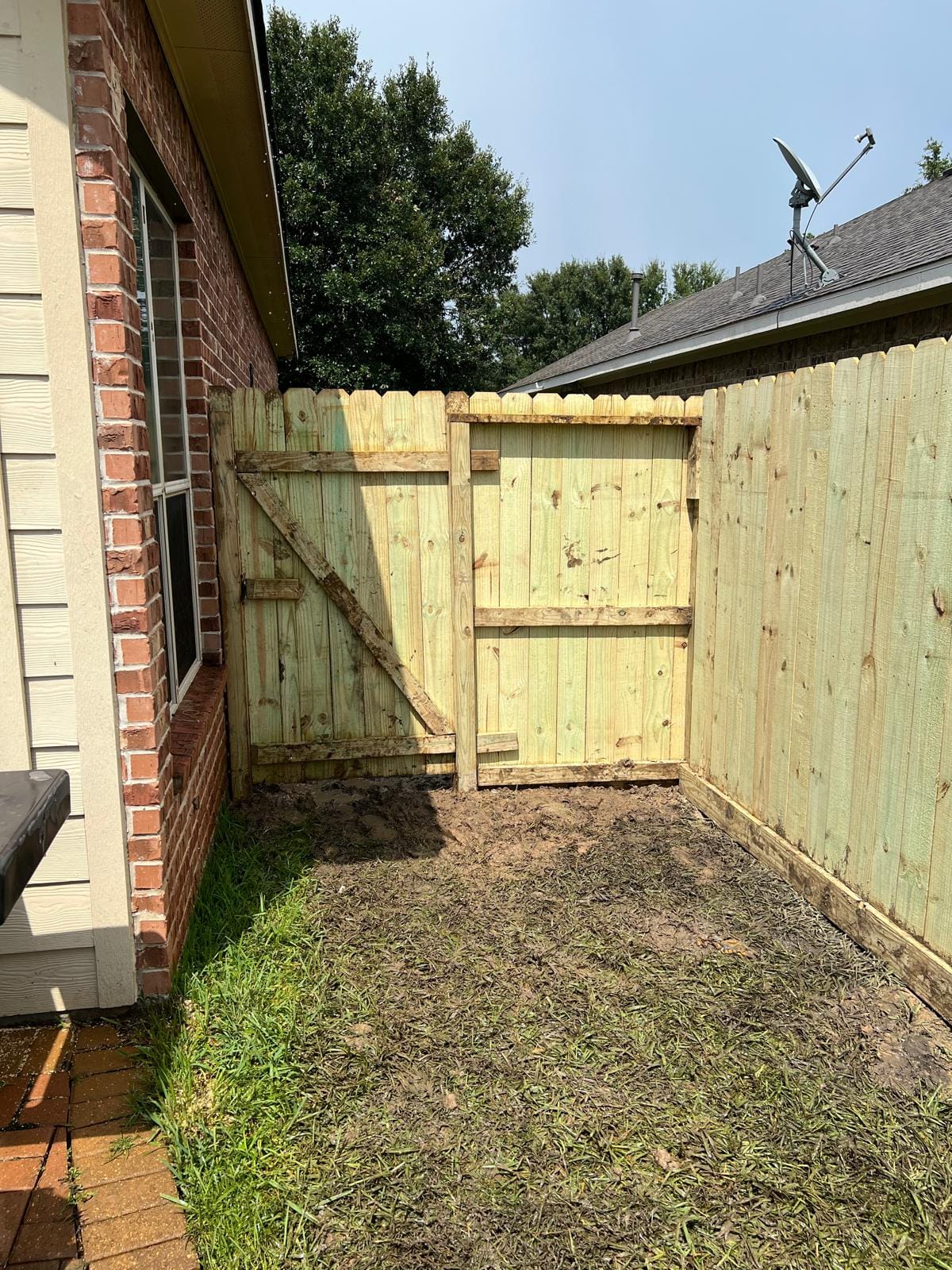 New light-toned wood fence and gate beside a brick house on freshly graded ground