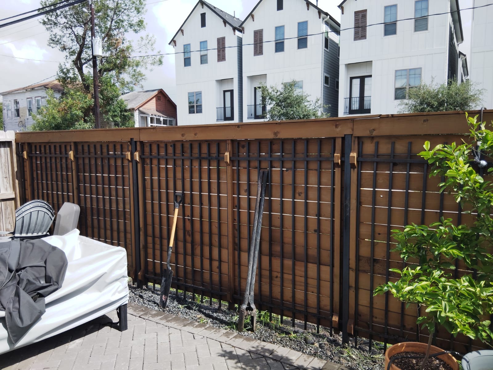 Dark-stained horizontal wood fence with black metal posts behind a row of townhouses