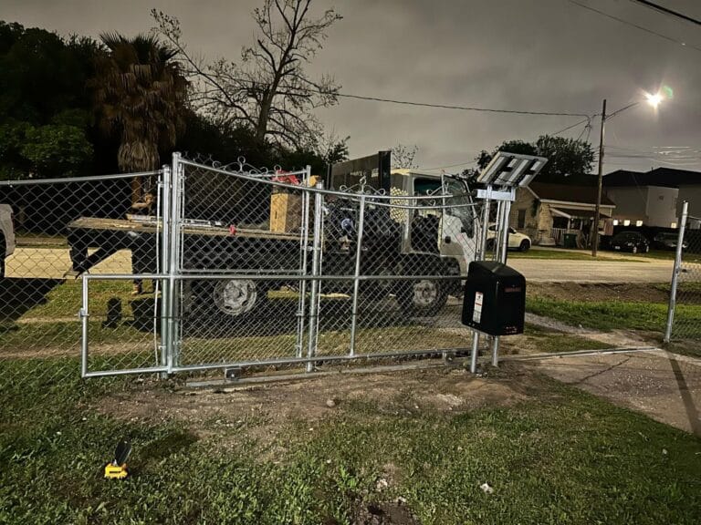 Galvanized chain link slide gate with a black gate operator and a solar panel on a post beside it, photographed at night with a work truck behind