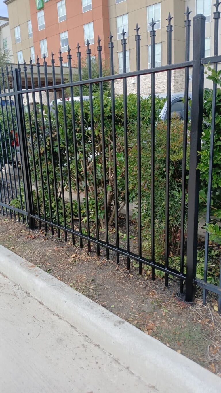 Black ornamental steel fence with spear-top pickets along a sidewalk in front of a multi-storey building