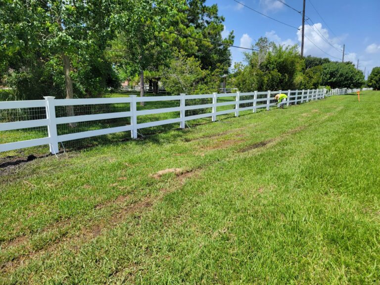 White rail ranch fence with wire backing running along a field