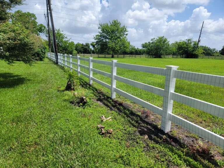 Long white three-rail ranch fence beside an open field