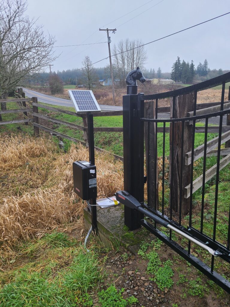 Solar-powered gate operator mounted beside a metal gate frame in a rural setting