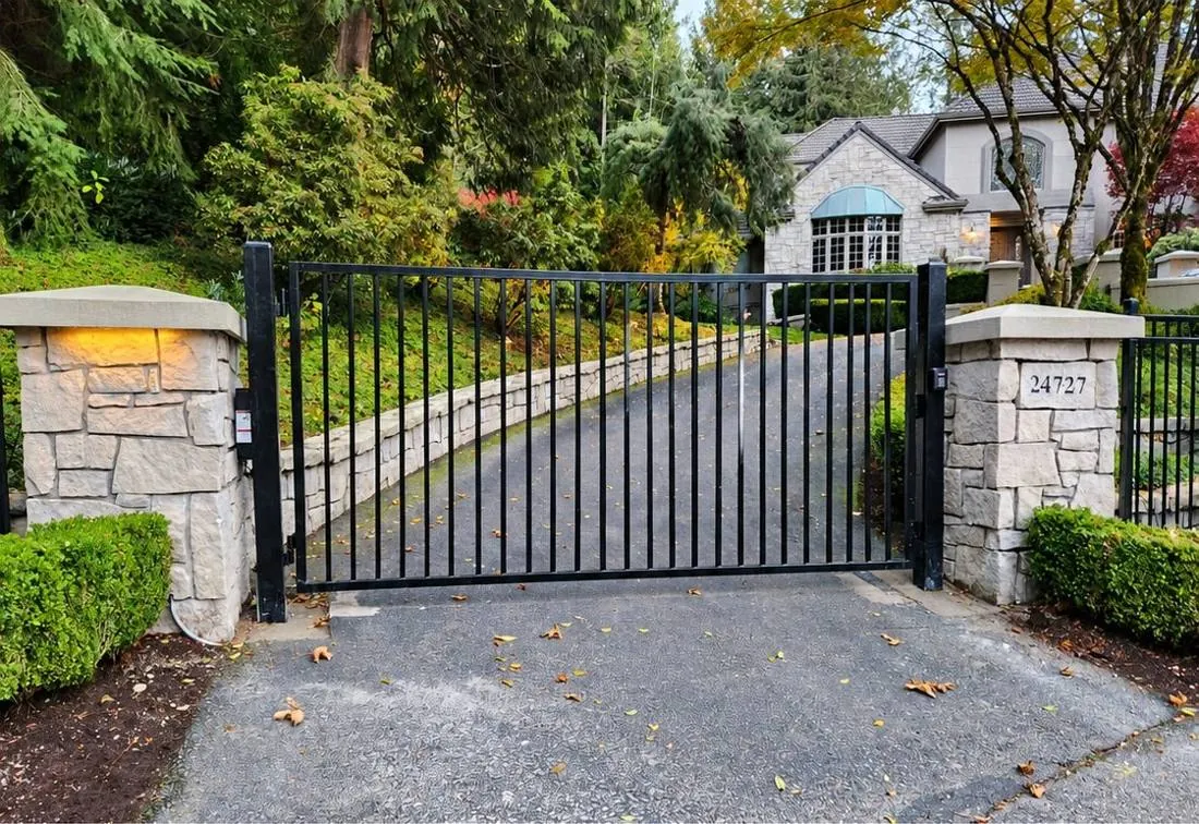 Arched iron driveway gate between stone pillars