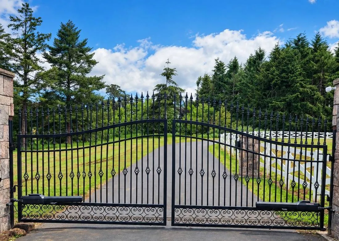 Arched iron gate with a scroll base across a long drive